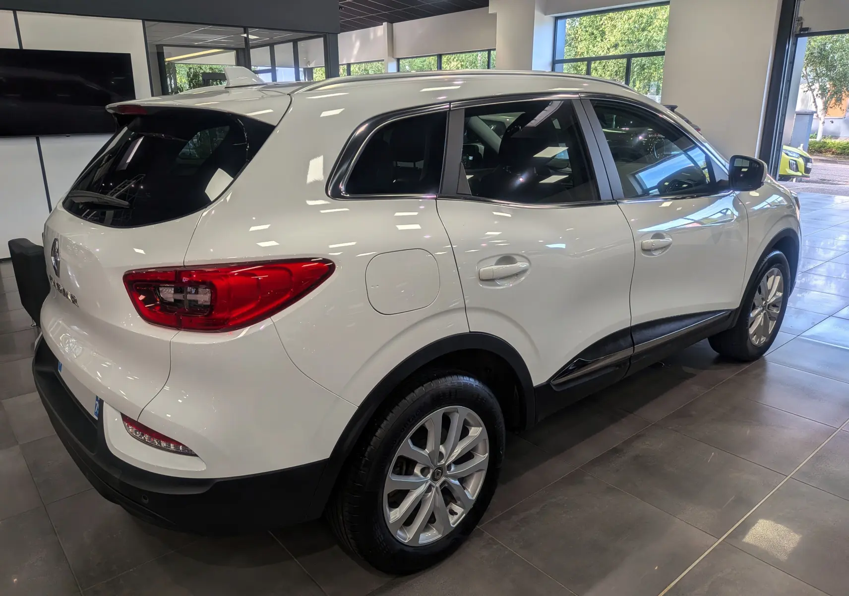 Renault Kadjar blanc glacier vu en 3/4 arrière droit dans un showroom lumineux avec jantes alliage et vitres teintées.