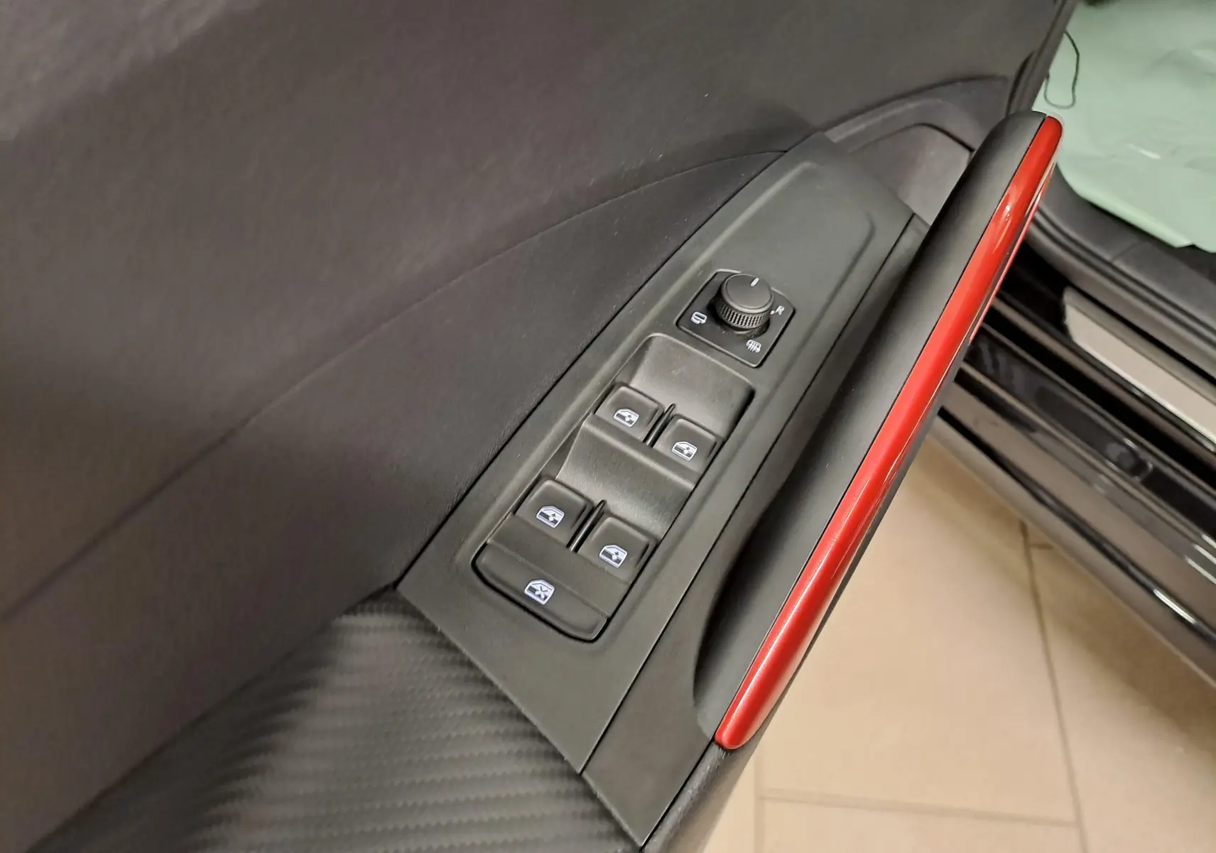 Détail de la porte côté conducteur de la Skoda Fabia 2024 noire avec commandes de vitres et insert rouge brillant.