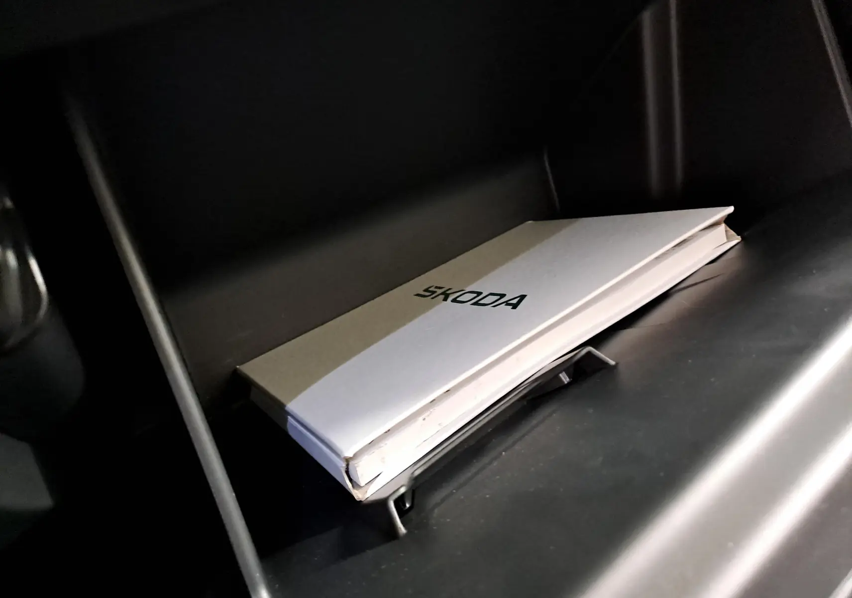 Manuel SKODA posé dans la boîte à gants sombre d'une Fabia 1.5 TSI 150 DSG7 Monte-Carlo noire.