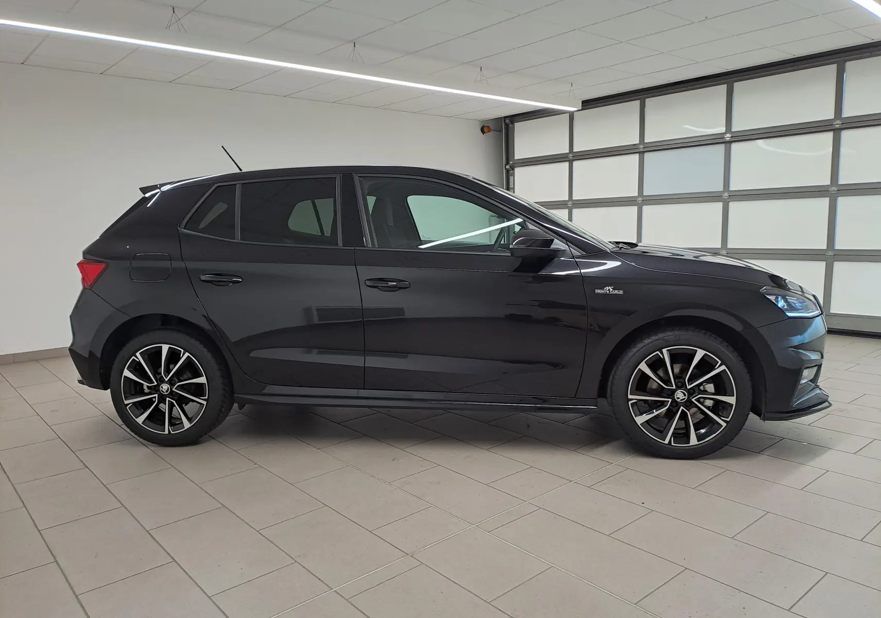 Profil côté gauche d'une Skoda Fabia 2024 noire Magic Nacré avec jantes alliage et finition Monte-Carlo visible en intérieur showroom.