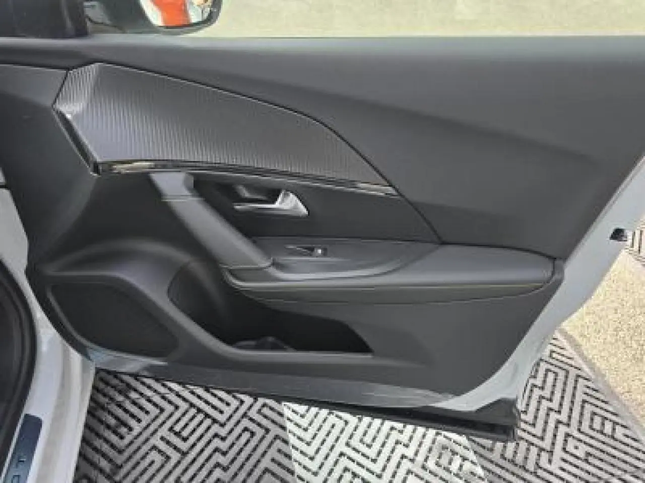 Porte côté gauche ouverte d’un Peugeot 2008 blanc Okenite, intérieur noir avec insert carbone et haut-parleur intégré.