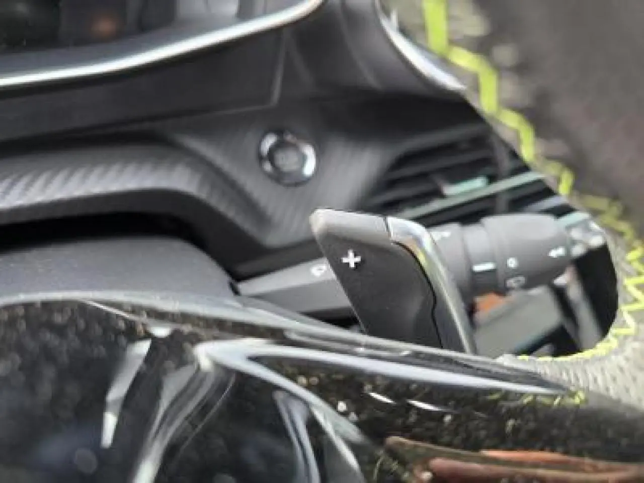 Gros plan sur la palette de changement de vitesse + du volant au cuir noir avec surpiqûres vertes du Peugeot 2008 hybride blanc.