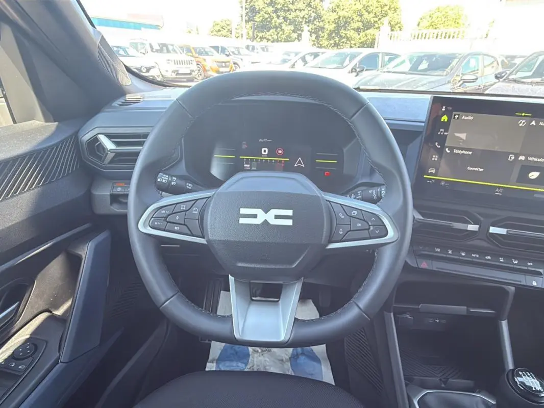 Vue intérieure centrée sur le volant multifonction et le tableau de bord numérique du Dacia Duster 2025.