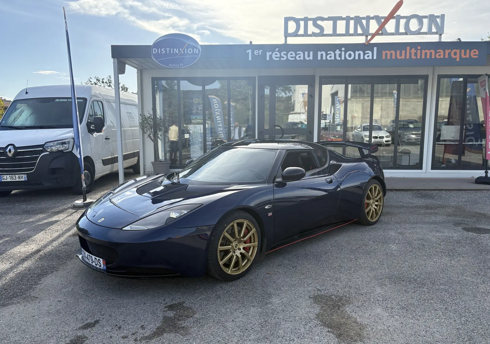 Lotus Evora 3.5 V6 S 2015 bleu Nightfall en 3/4 avant droit avec jantes dorées et aileron arrière visible.
