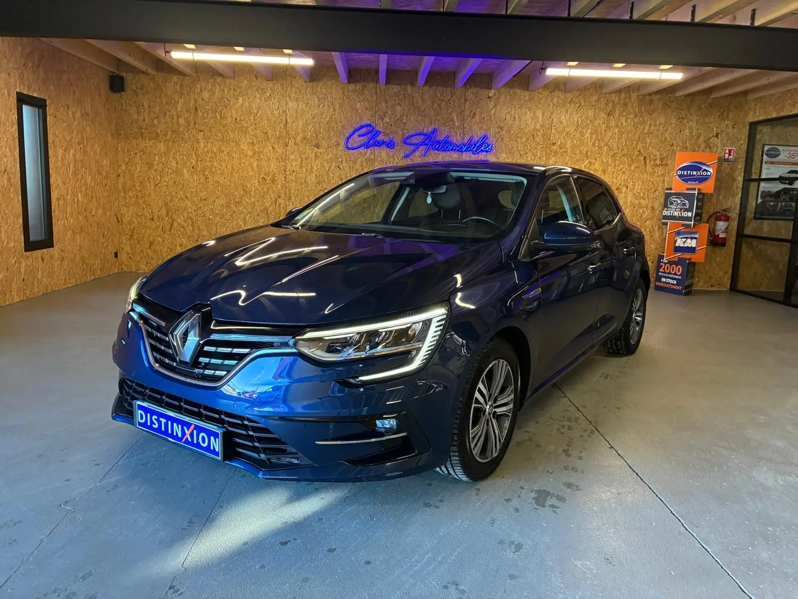 Renault Mégane bleu 3/4 avant droit en intérieur, avec phares LED allumés et jantes alliage bicolores.