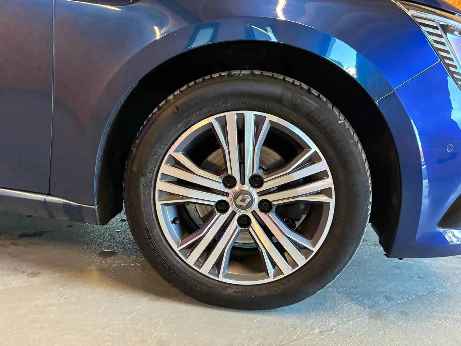 Gros plan sur la roue avant gauche d'une Renault Mégane bleu 2021 avec jante alliage bicolore et logo central Renault.