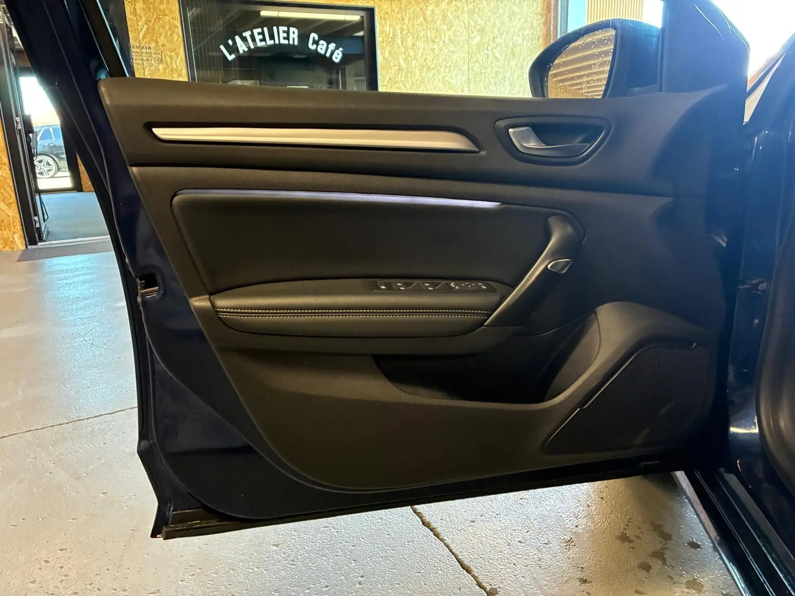 Vue rapprochée de la porte côté gauche ouverte d'une Renault Mégane bleu 2021, avec garniture intérieure noire et commandes électriques.