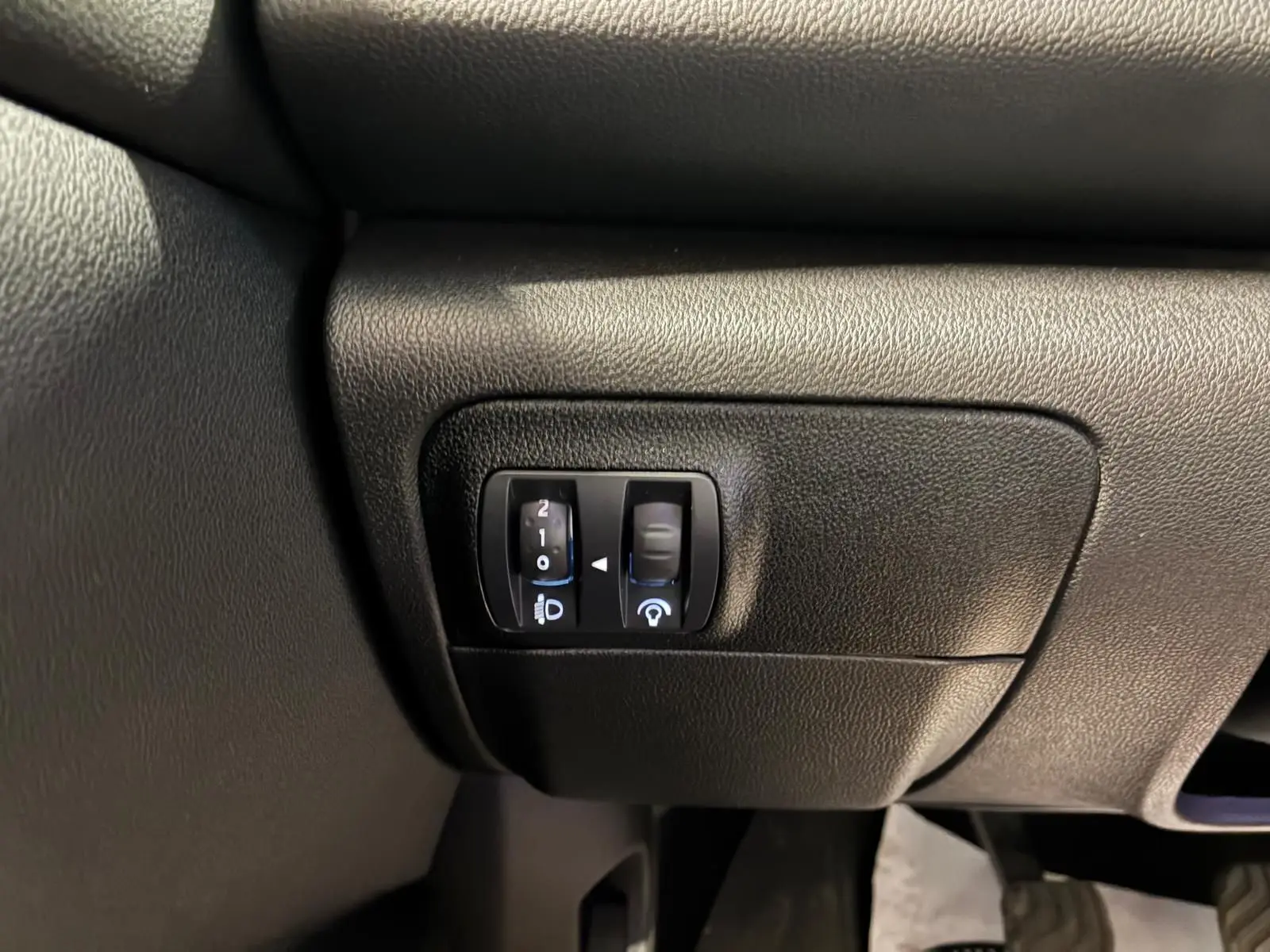Gros plan sur les commandes de réglage des phares et du tableau de bord dans une Renault Mégane 1.5 DCI 115 Intens 2021.