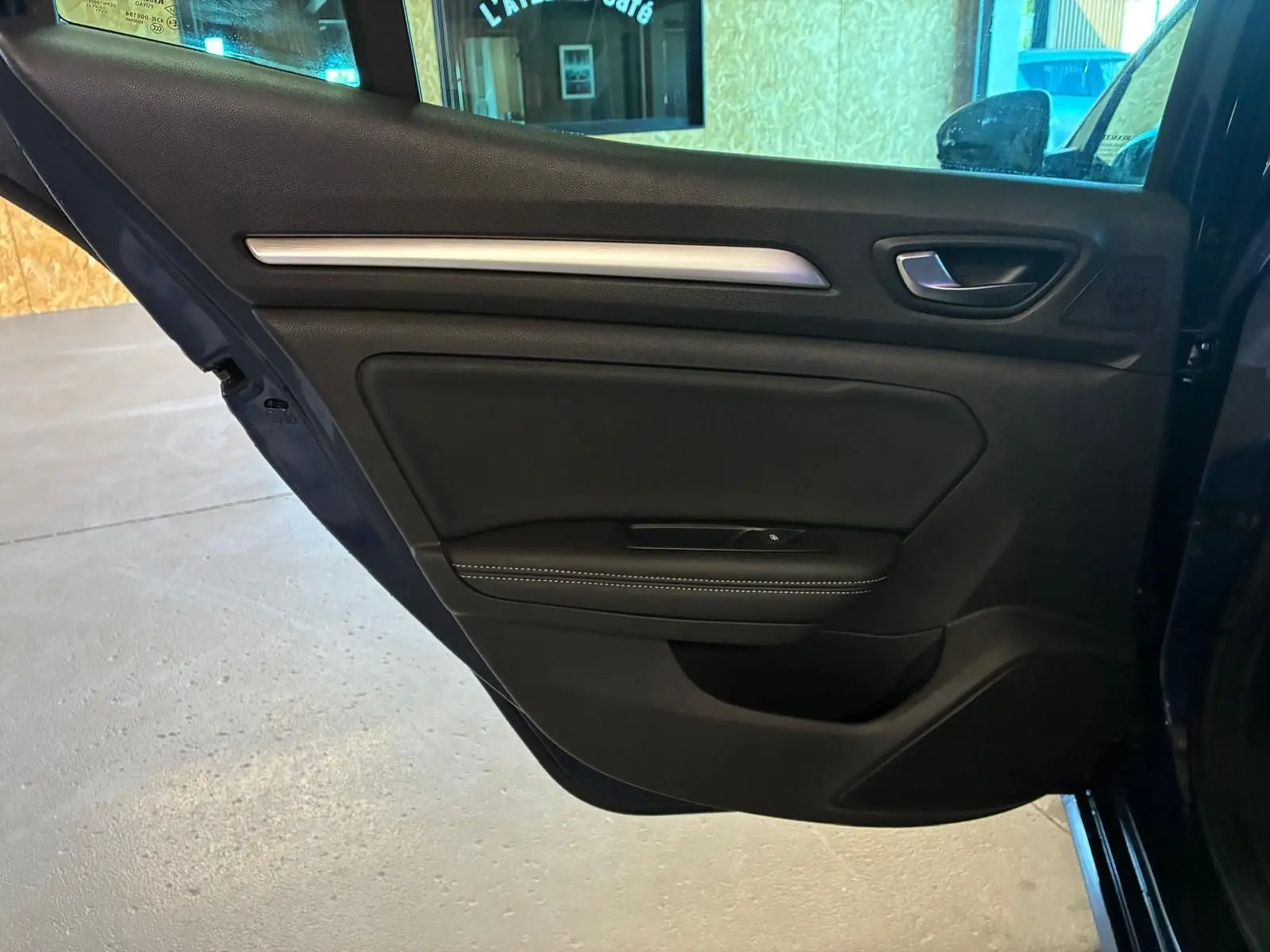Vue rapprochée de la porte arrière gauche bleu foncé d'une Renault Mégane 1.5 DCI 115 Intens 2021 avec garniture noire et surpiqûres blanches.