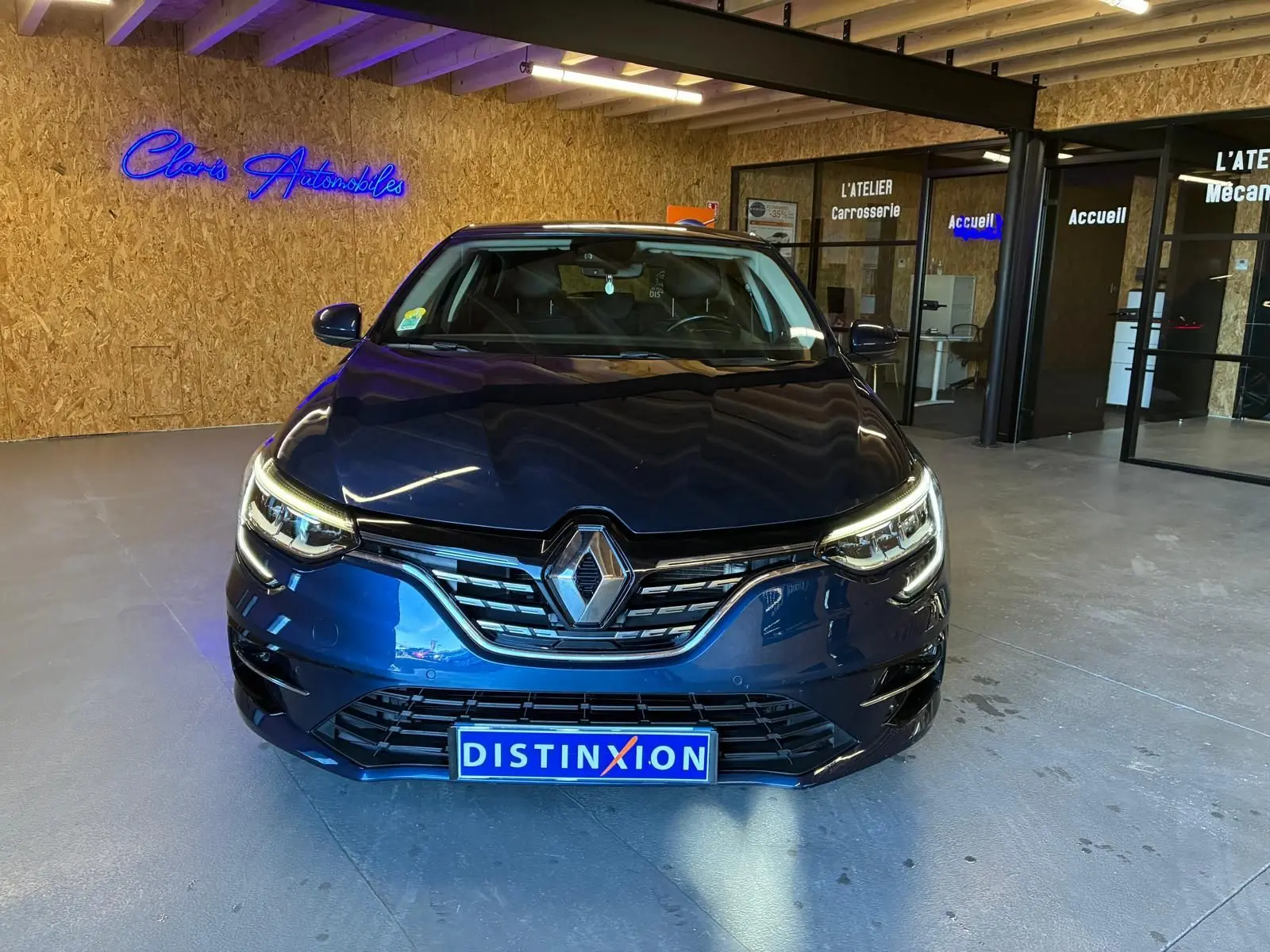 Vue frontale d'une Renault Mégane 1.5 dCi 115 Intens bleu, avec phares allumés dans un showroom moderne.