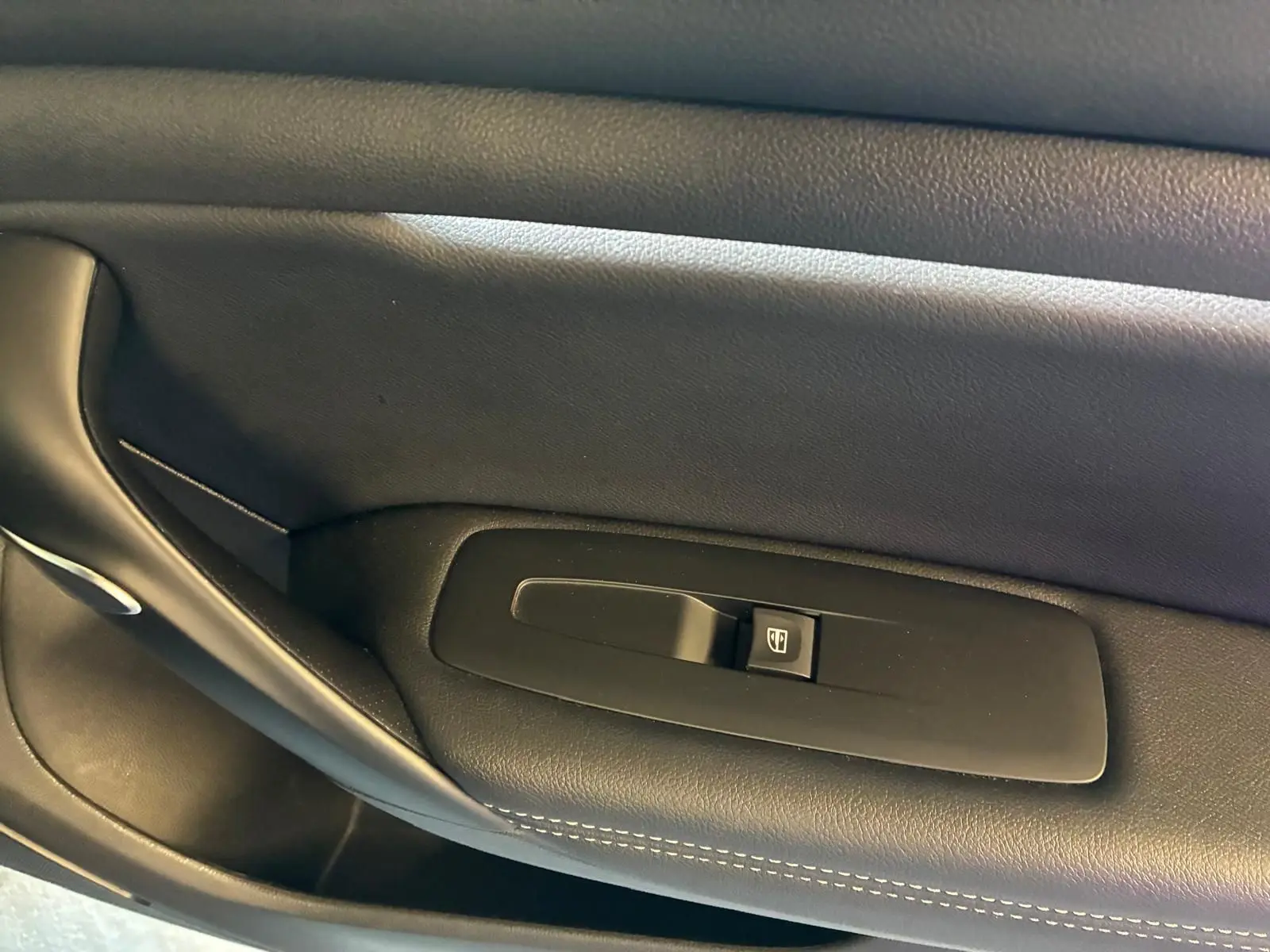 Gros plan sur la commande de lève-vitre côté gauche en plastique noir avec surpiqûres blanches sur la garniture intérieure.