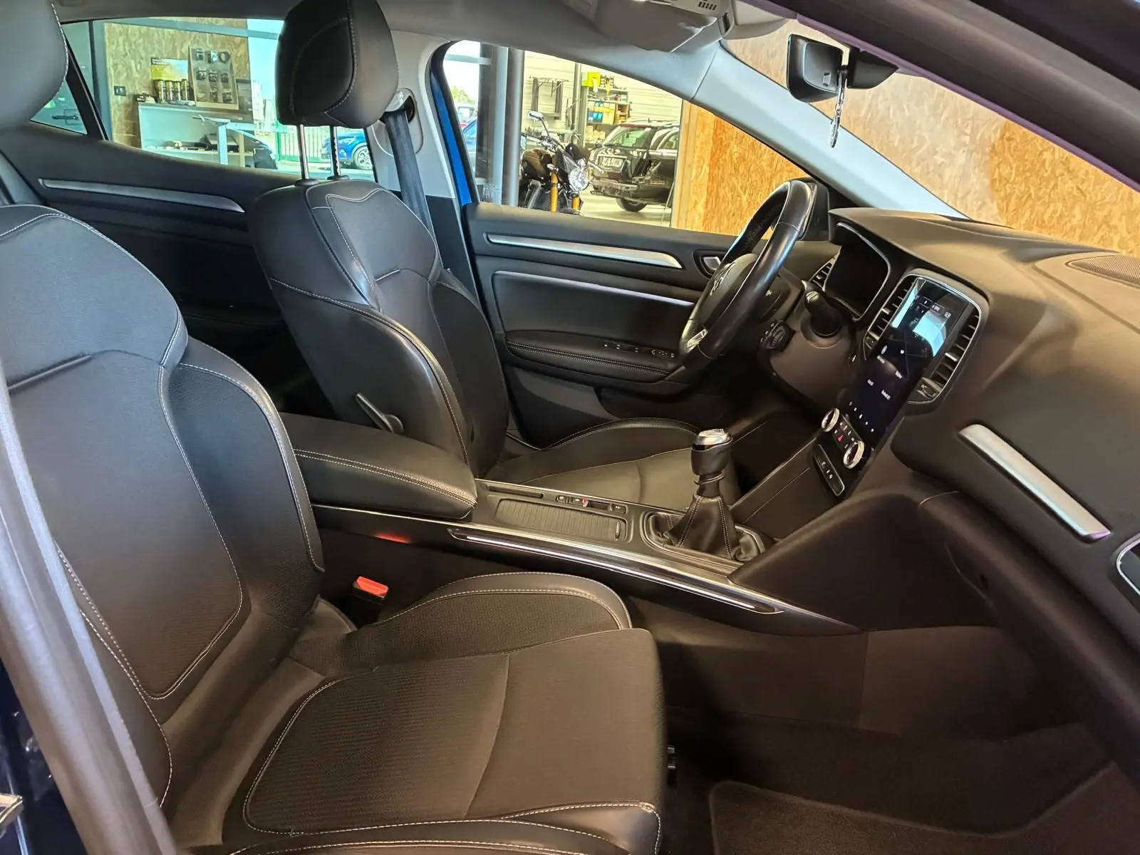 Intérieur avant de la Renault Mégane bleu 2021, sièges cuir noir, tableau de bord avec écran tactile et boîte manuelle.
