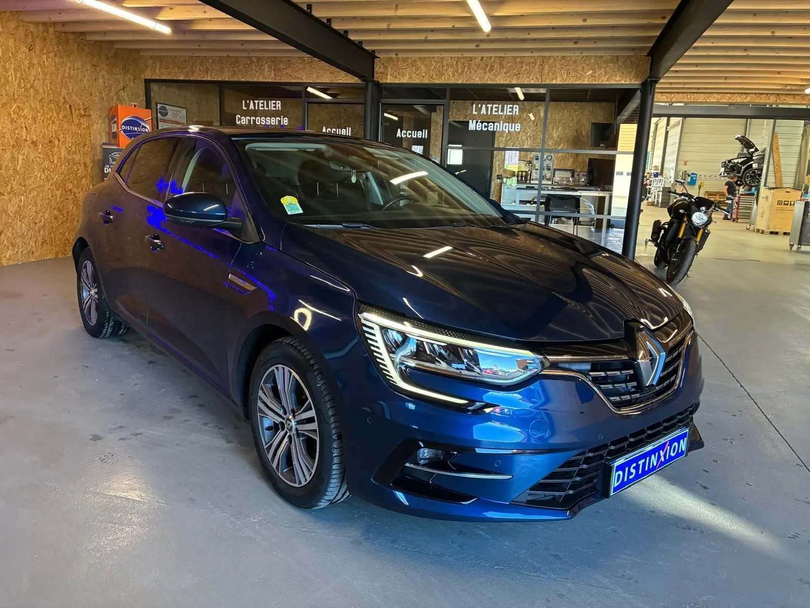 Renault Mégane 1.5 DCI 115 Intens bleu vue 3/4 avant droit dans un garage avec éclairage intérieur.