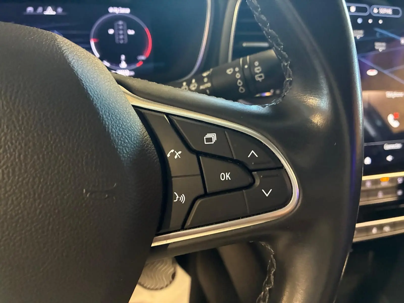 Gros plan sur les commandes au volant en cuir noir de la Renault Mégane 1.5 DCI 115 Intens, tableau de bord numérique en arrière-plan.