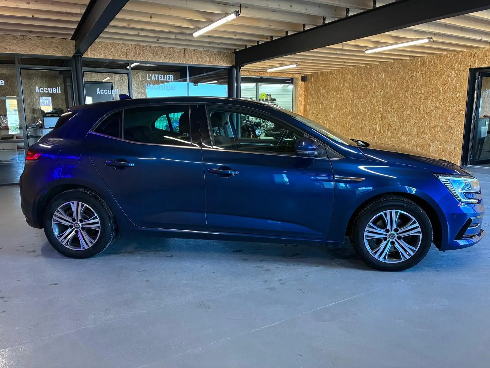 Profil droit d'une Renault Mégane 1.5 DCI 115 Intens bleu 2021 avec jantes alliage bicolores en intérieur d'atelier.
