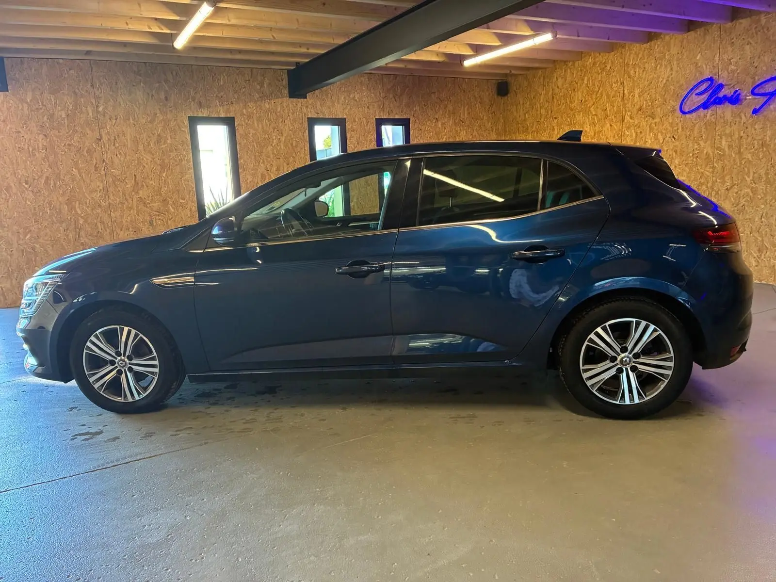 Profil côté gauche d'une Renault Mégane 1.5 dCi 115 Intens bleu, en intérieur avec jantes alliage bicolores visibles.