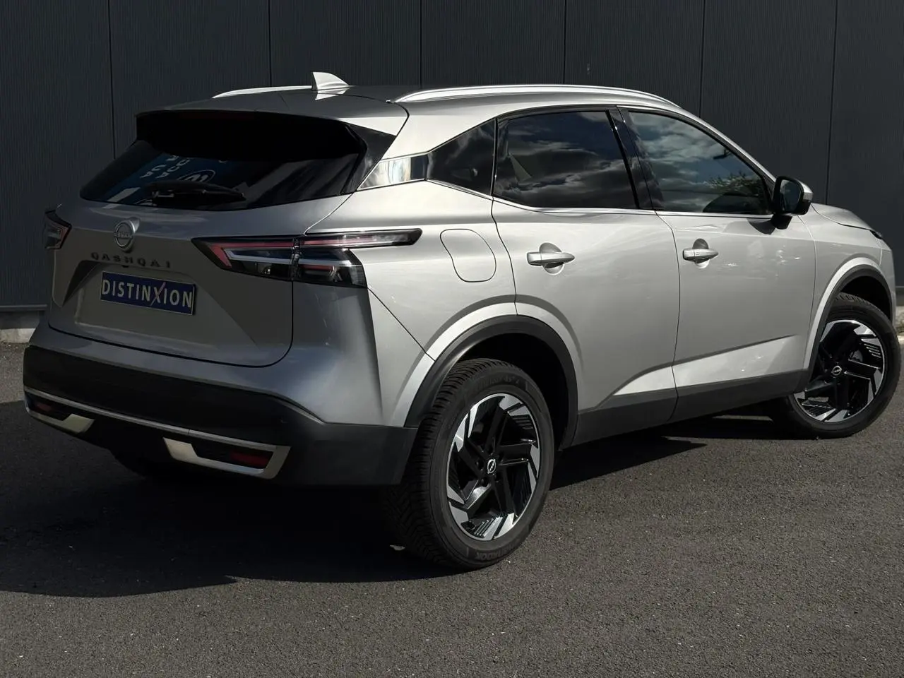 Nissan Qashqai gris argent vu en 3/4 arrière droit, avec hayon électrique et jantes alliage noires.