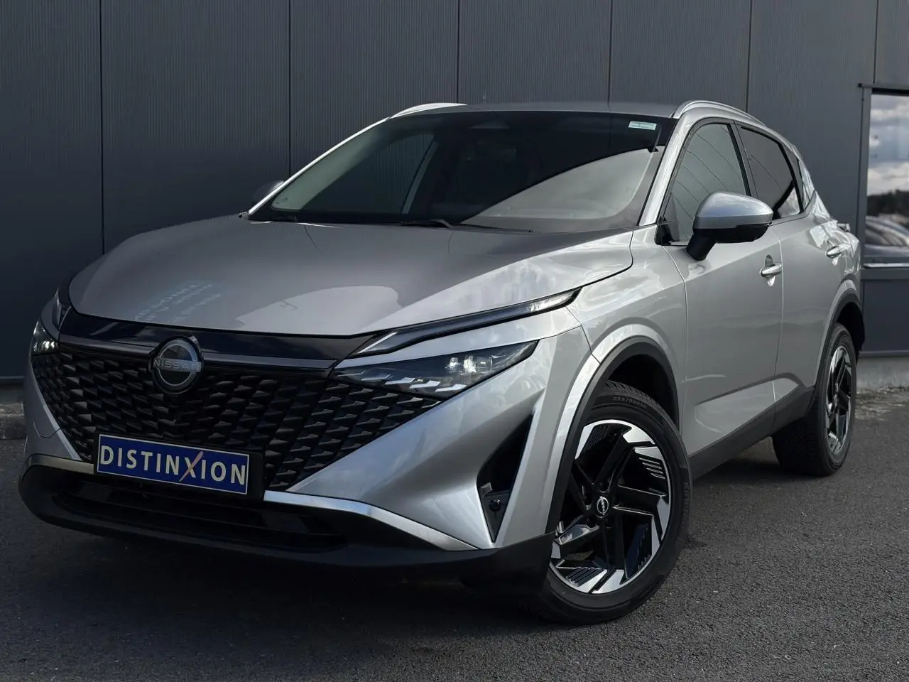 Nissan Qashqai gris argent vu en 3/4 avant droit avec calandre noire et jantes alliage 18 pouces.