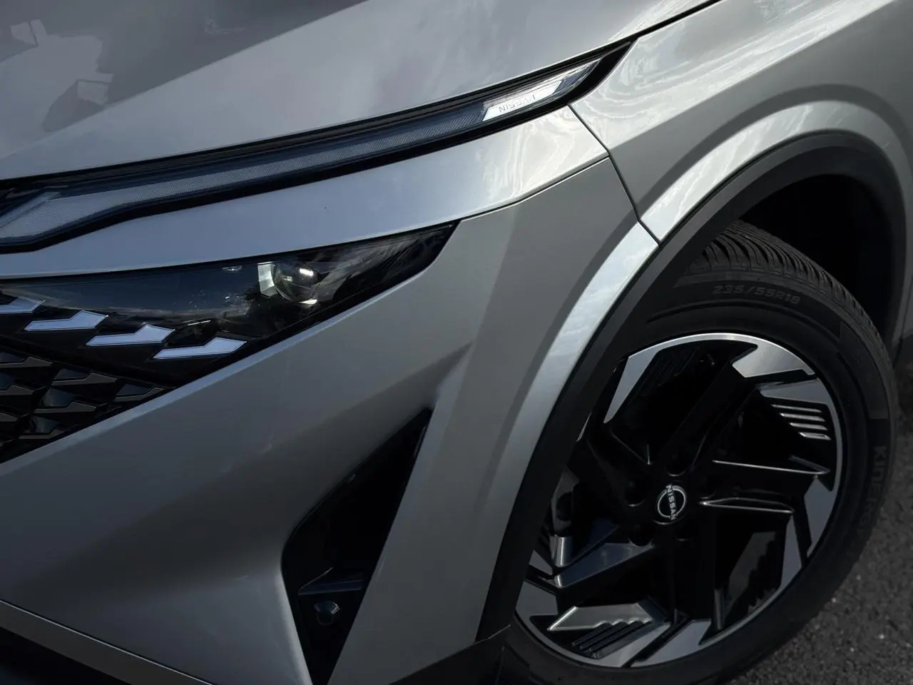 Gros plan sur l'avant droit gris argent du Nissan Qashqai 2025, mettant en valeur le phare LED et la jante alliage noire.