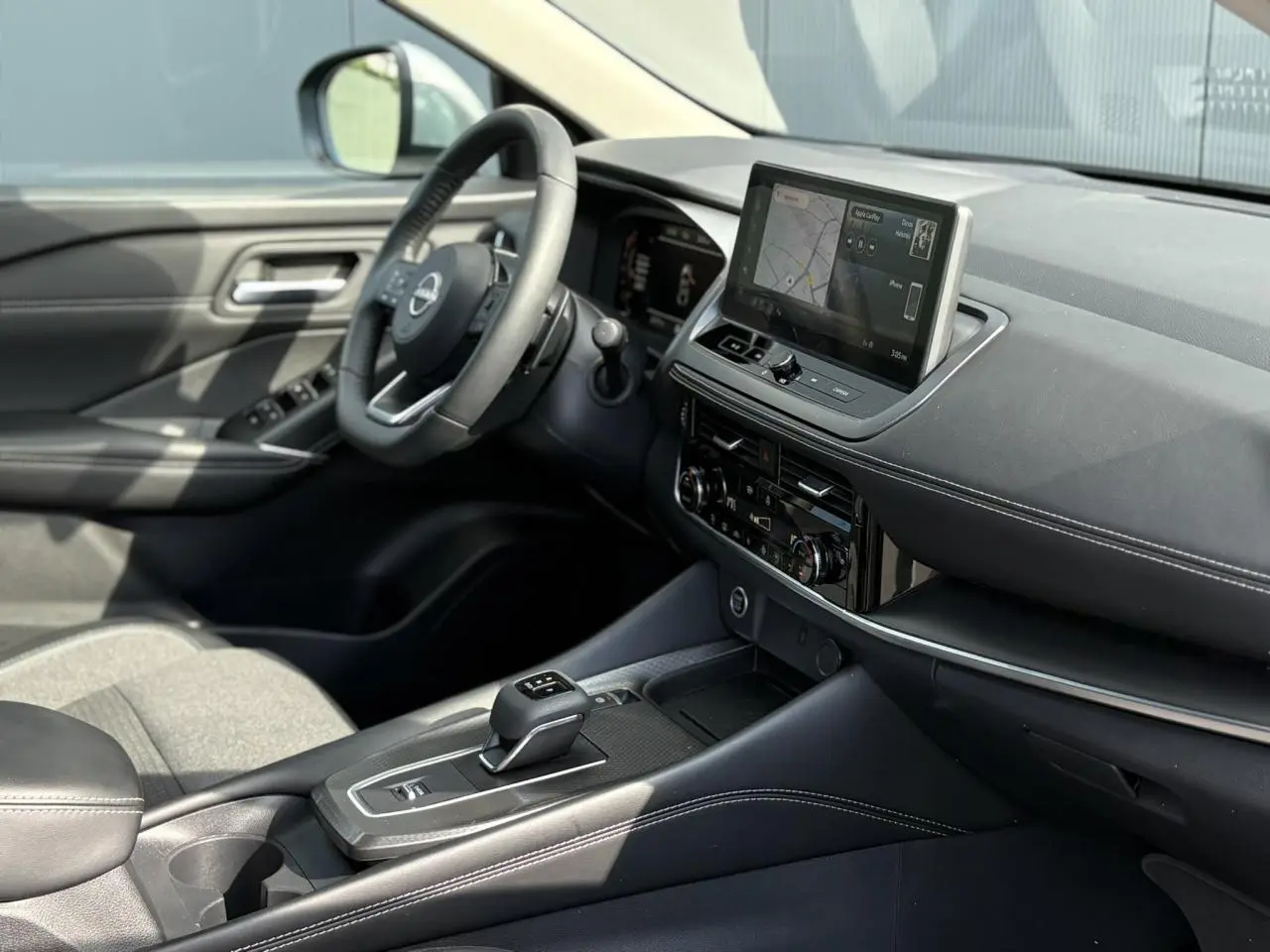 Intérieur du Nissan Qashqai 2025 vu côté conducteur, avec tableau de bord noir et écran tactile central.