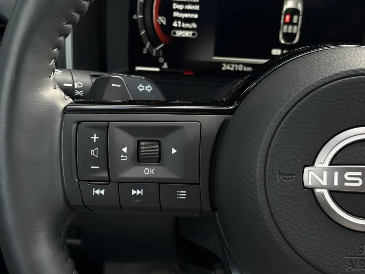 Gros plan sur les commandes au volant gauche du Nissan Qashqai gris argent 2025 avec affichage numérique en arrière-plan.