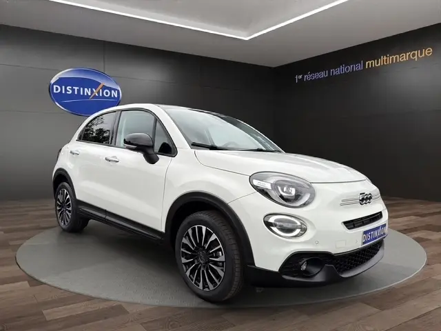 Vue 3/4 avant droit d'une FIAT 500X blanche avec jantes noires et détails noirs contrastants dans un showroom.