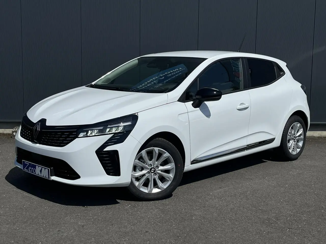 Renault Clio 2025 blanc glacier en 3/4 avant droit, avec jantes 16'' Boavista et rétroviseurs noirs électriques.