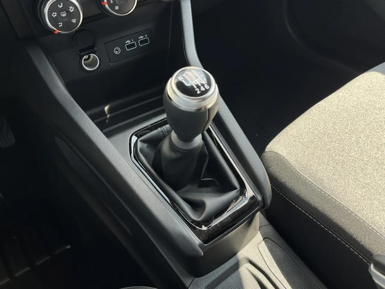 Gros plan sur la commande de boîte manuelle noire et la console centrale de la Renault Clio 2025, intérieur tissu gris.