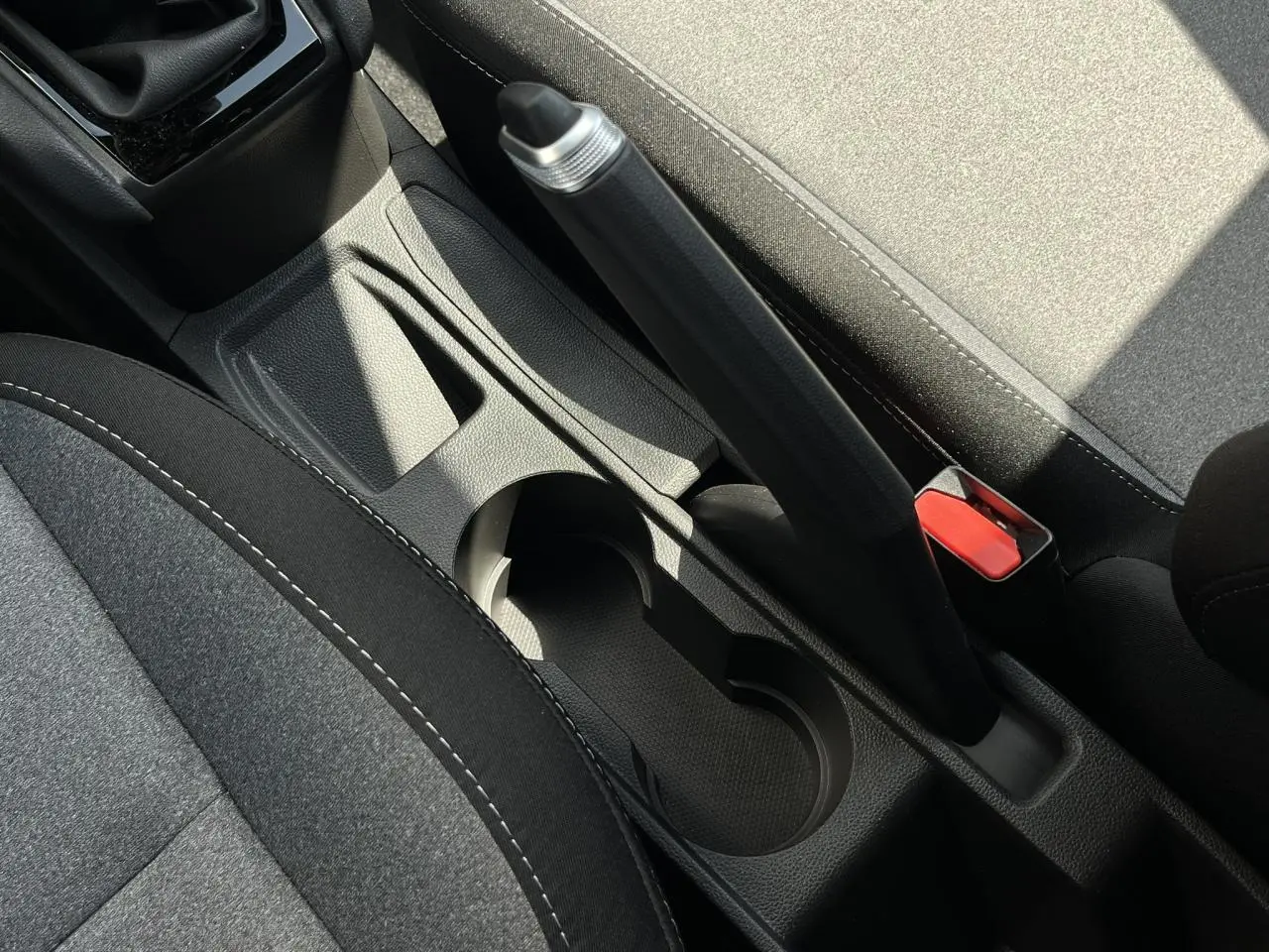 Gros plan sur la console centrale et frein à main de la Renault Clio 2025, sièges tissu gris et noir visibles.