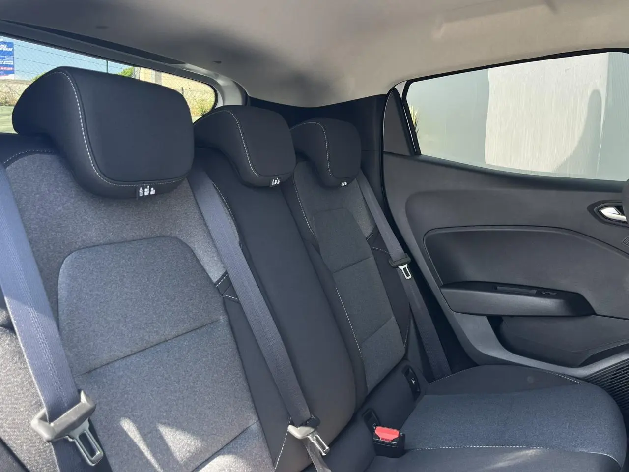 Vue côté droit de l'habitacle arrière de la Renault Clio 2025, sièges tissu gris foncé avec surpiqûres blanches.