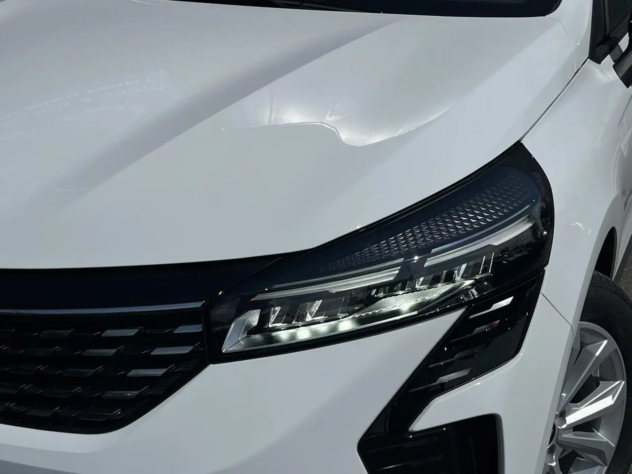 Gros plan sur le phare avant droit et la calandre noire d'une Renault Clio blanche Glacier avec jante 16 pouces.