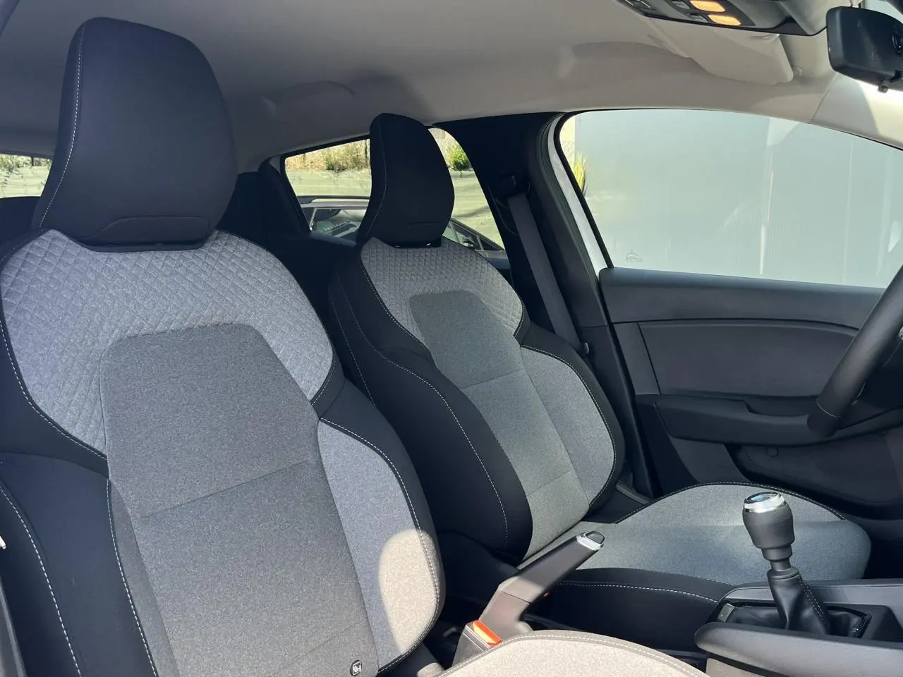 Intérieur de Renault Clio 2025 vu côté droit, sièges tissu gris et noir avec couture blanche et levier de vitesse manuel.