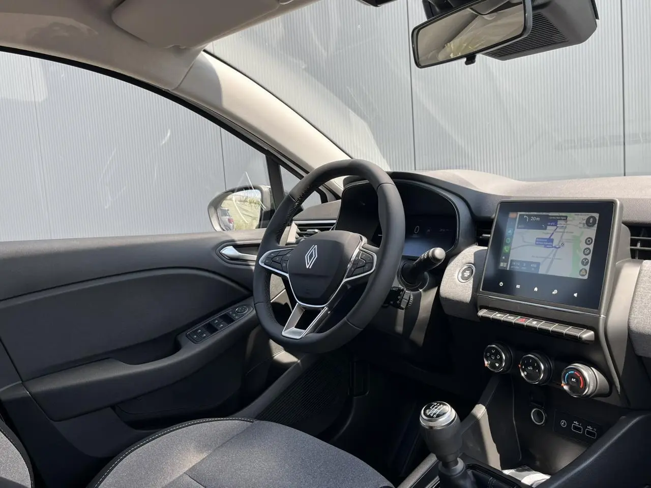 Intérieur de la Renault Clio 2025 vu côté conducteur, avec tableau de bord noir et écran tactile central affichant la navigation.