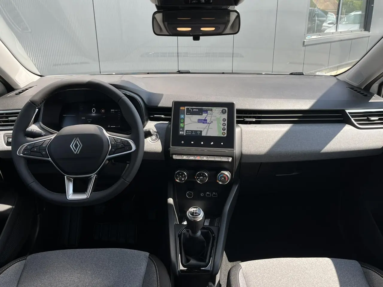 Vue intérieure avant de la Renault Clio 2025, tableau de bord moderne avec écran tactile et volant multifonction noir.