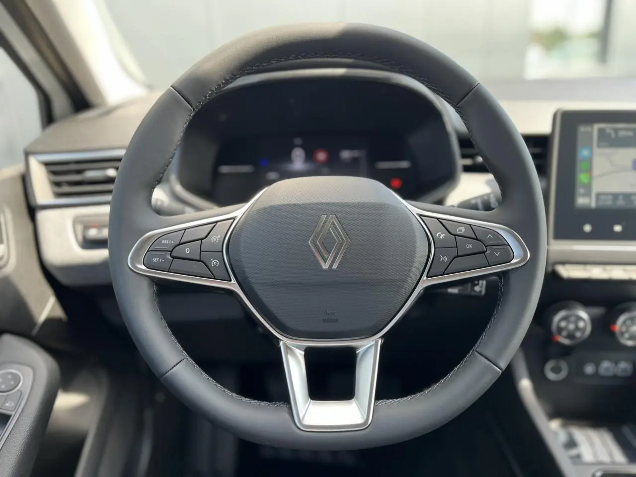 Volant cuir noir Renault Clio 2025 vu de face, avec commandes multifonctions et tableau de bord numérique flou.