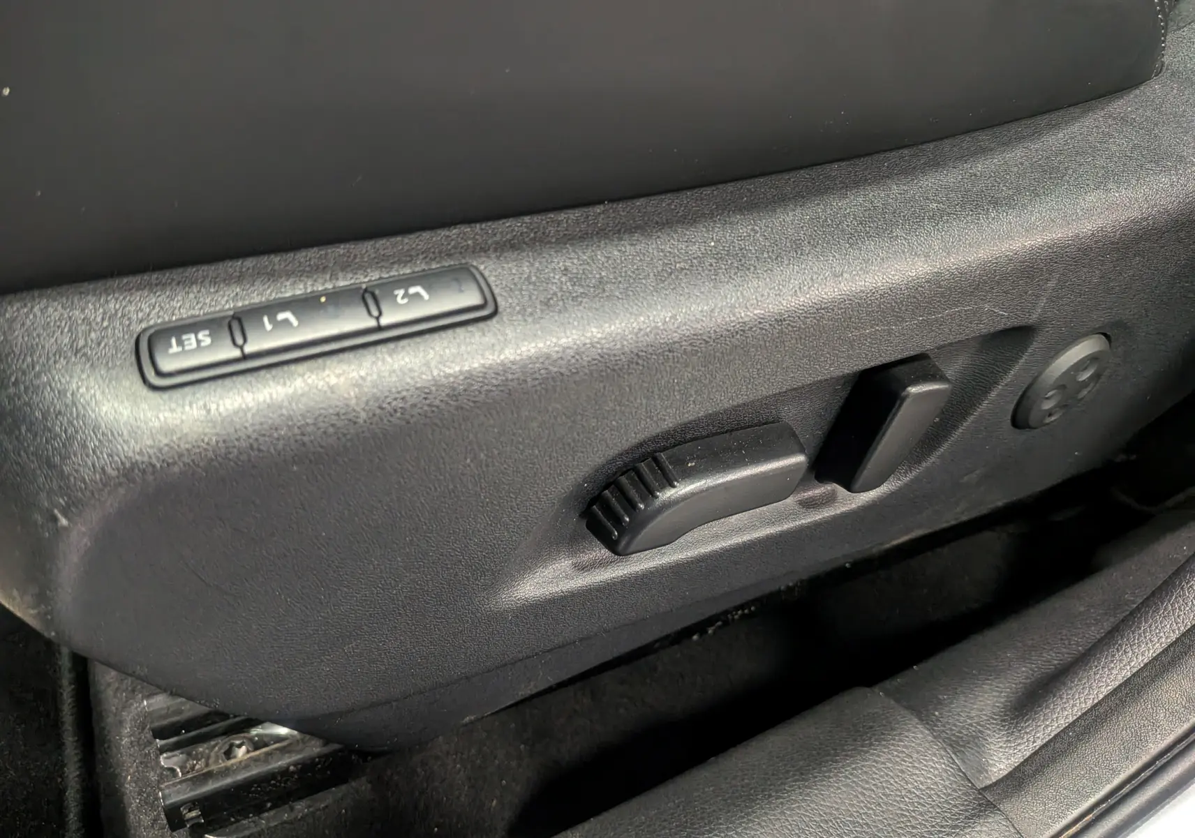 Gros plan sur les commandes de réglage électrique du siège conducteur noir dans un Nissan Qashqai 2018 gris perle.