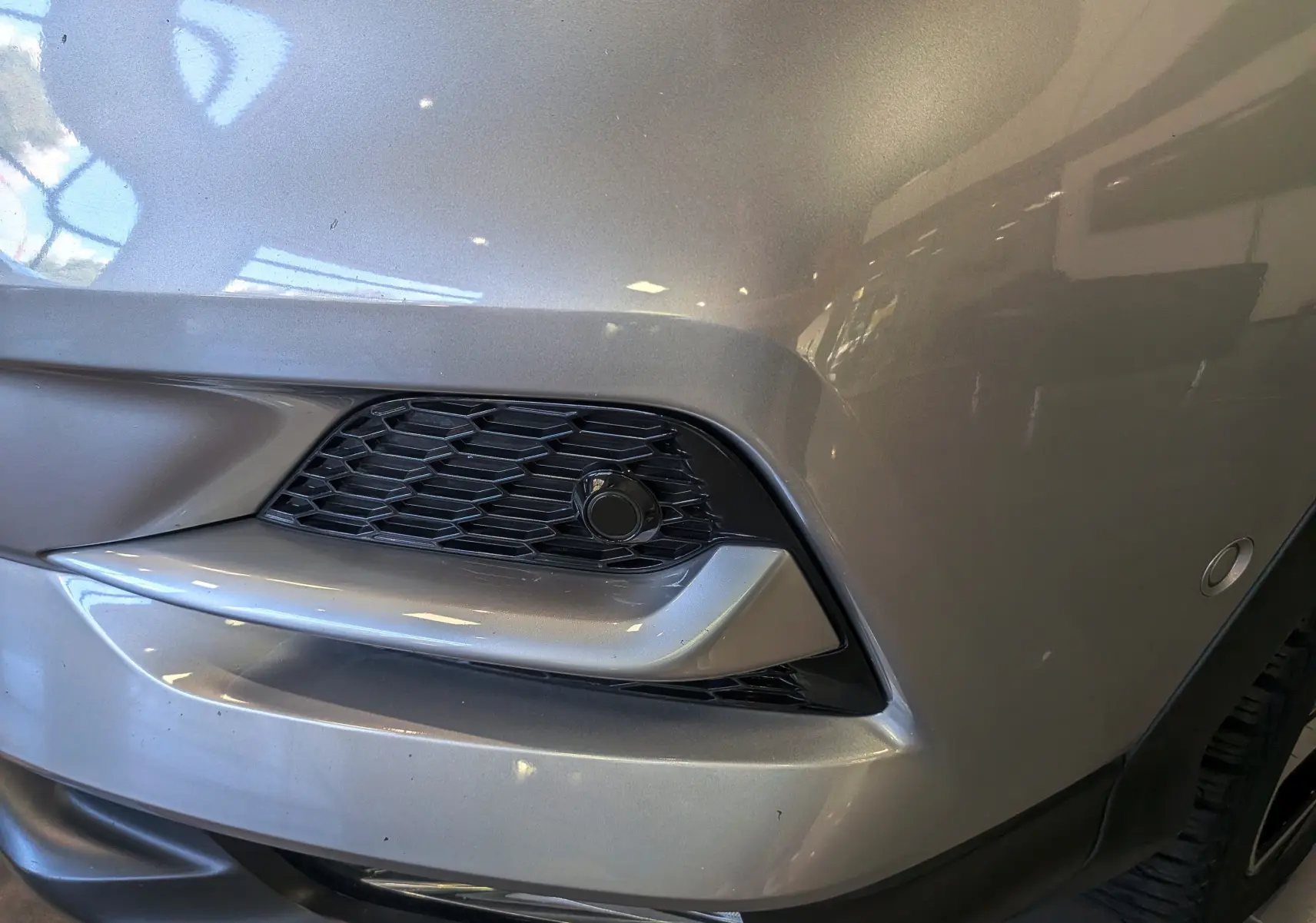 Gros plan sur l'angle avant droit du Nissan Qashqai gris perle, mettant en valeur la calandre et le capteur de stationnement.