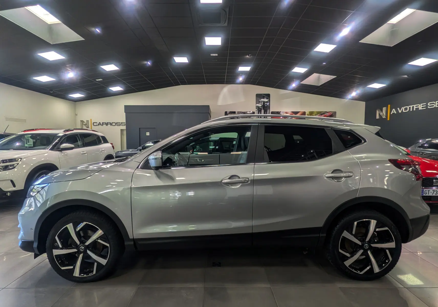 Profil côté gauche d'un Nissan Qashqai gris perle 2018 avec jantes alliage bicolores en showroom.
