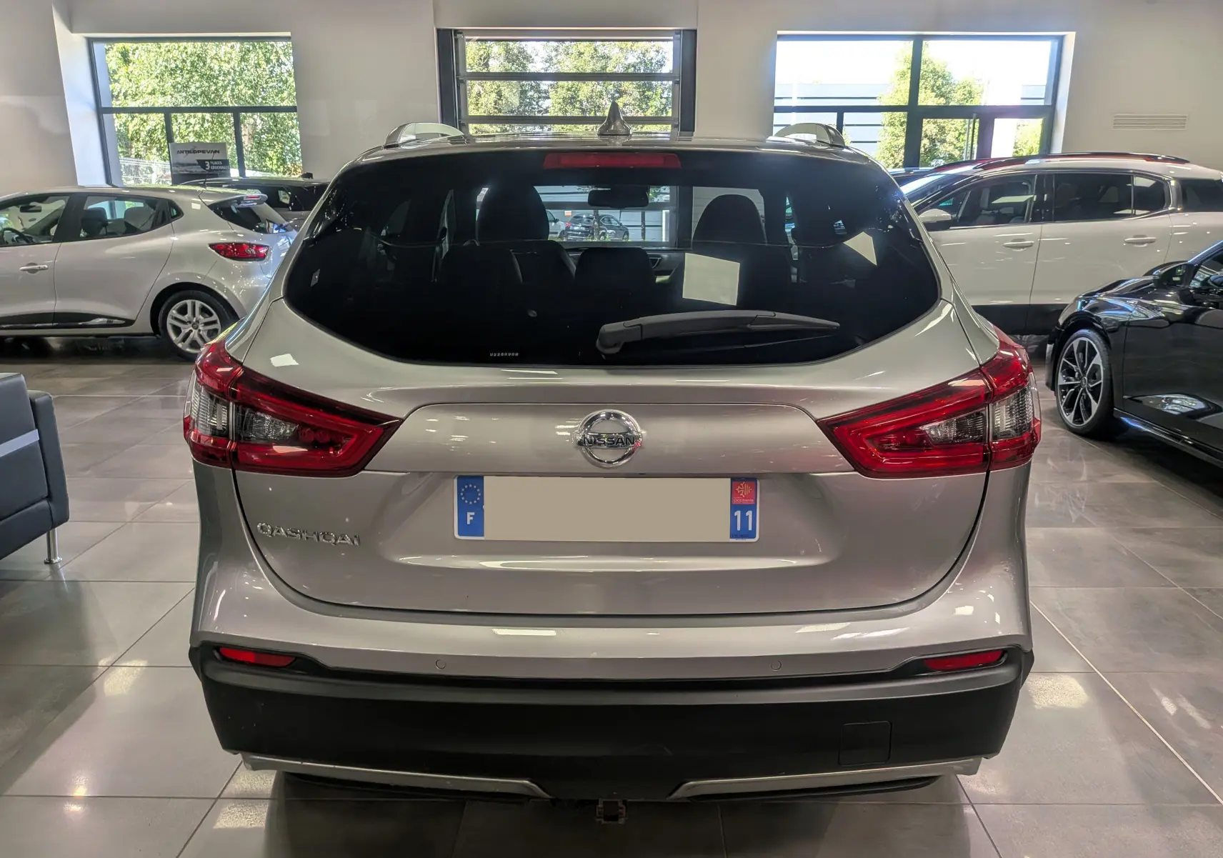 Vue arrière d'un Nissan Qashqai gris perle 2018 en showroom, avec feux arrière rouges et lunette arrière teintée.
