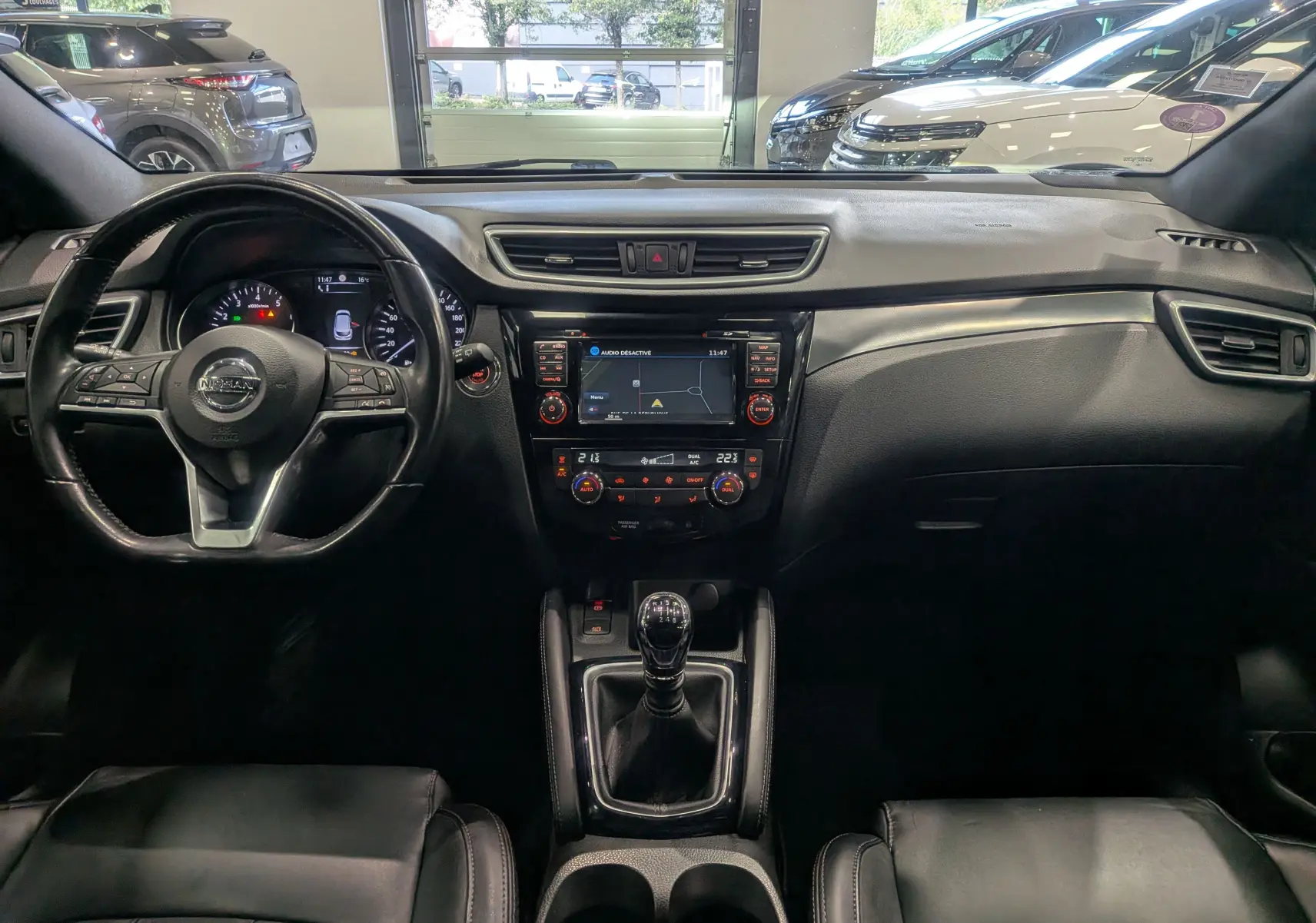 Vue intérieure frontale du Nissan Qashqai 2018, tableau de bord noir avec écran central et boîte manuelle.