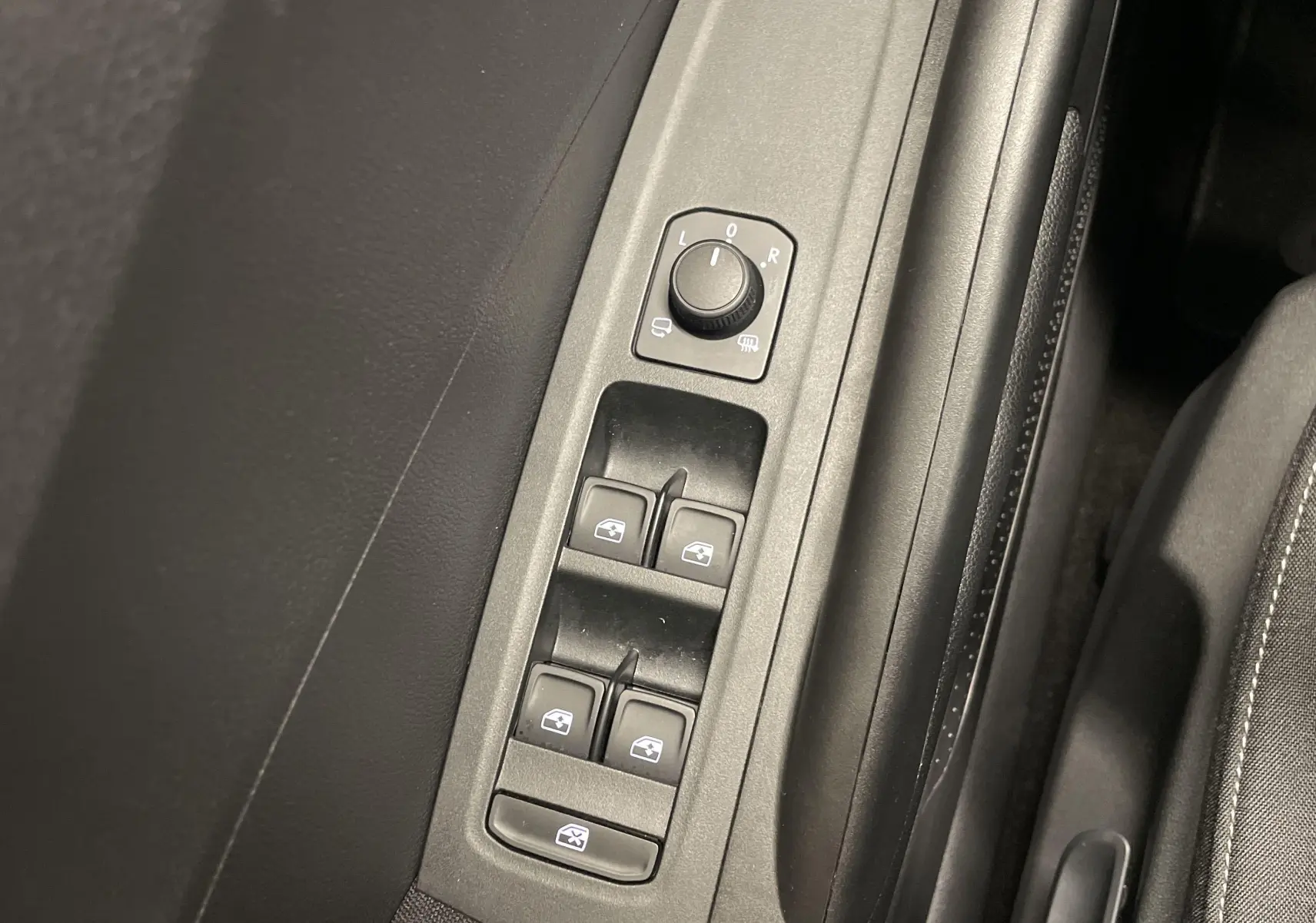 Gros plan sur les commandes des vitres électriques et réglage des rétroviseurs côté conducteur d'une Skoda Fabia gris argent.