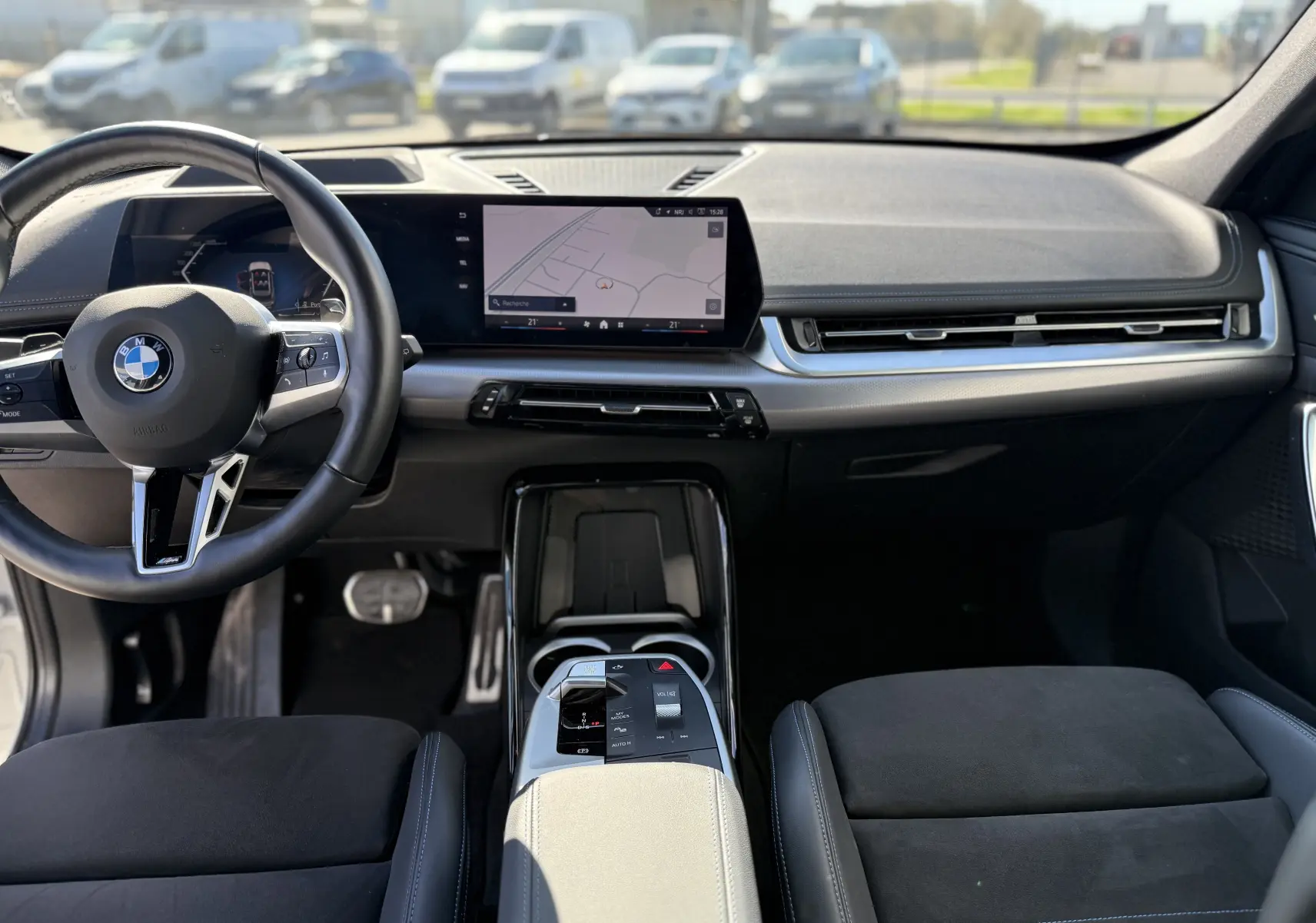 Vue intérieure avant du BMW X1 20D 2025 avec tableau de bord moderne, écran tactile et volant multifonction noir.