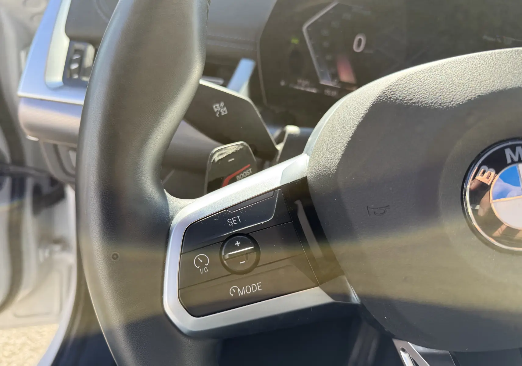 Gros plan sur le volant noir de la BMW X1 blanc minéral, mettant en valeur les commandes de régulateur de vitesse côté gauche.