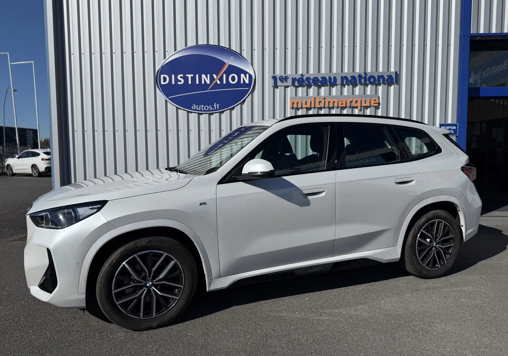 BMW X1 blanc minéral vue de profil côté gauche, avec jantes noires et badge M Sport visible sur aile avant.