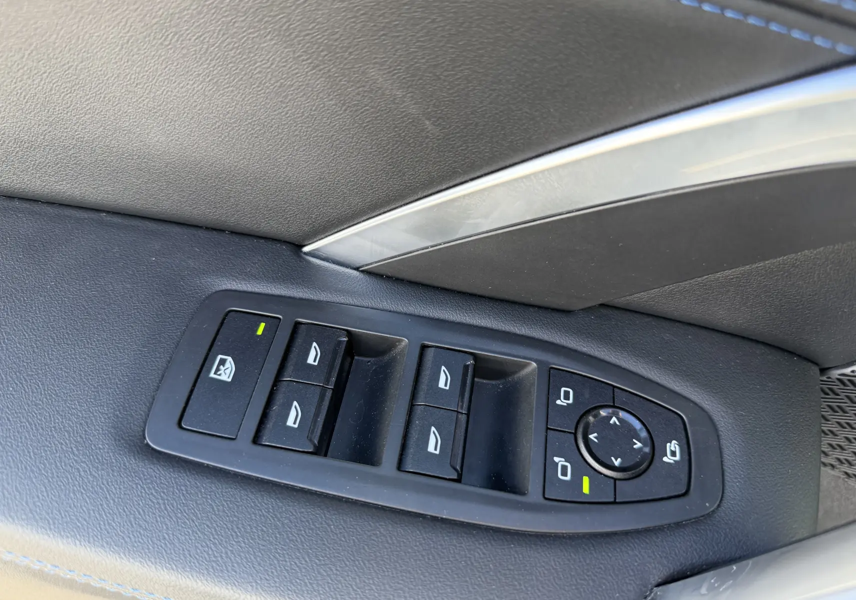 Gros plan sur les commandes des vitres et rétroviseurs côté gauche intérieur d'un BMW X1 blanc Mineral 2025.