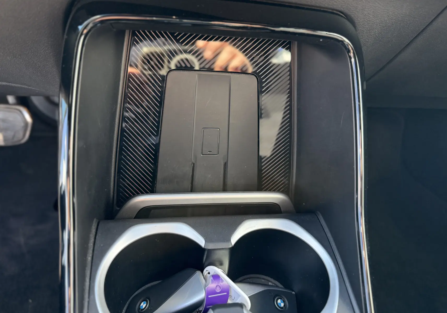 Gros plan sur la console centrale du BMW X1 20D 2025, avec porte-gobelets et surface noire brillante à motifs.