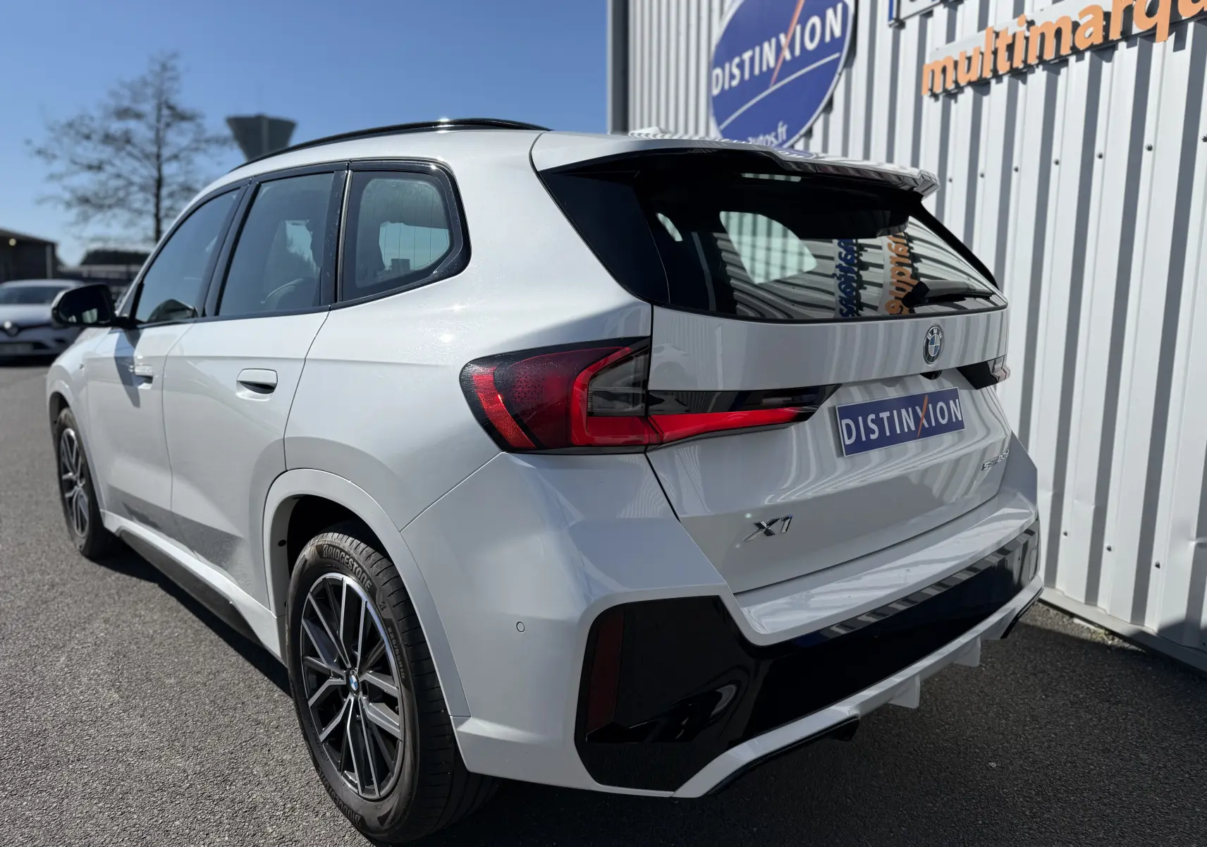 BMW X1 blanc minéral vue 3/4 arrière droit, avec feux arrière LED et jantes alliage noires contrastées.