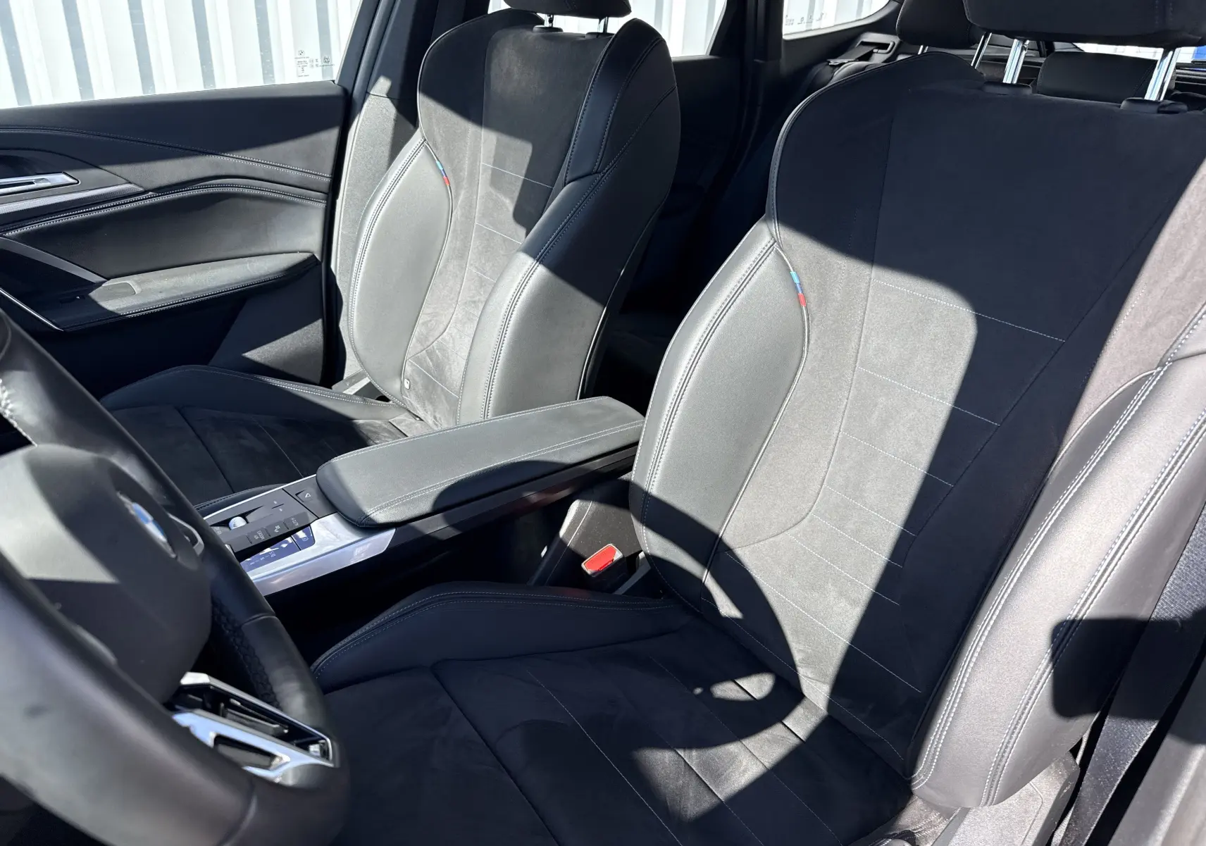 Vue intérieure rapprochée des sièges avant en cuir noir avec surpiqûres et détails tricolores BMW d’un X1 blanc mineral.