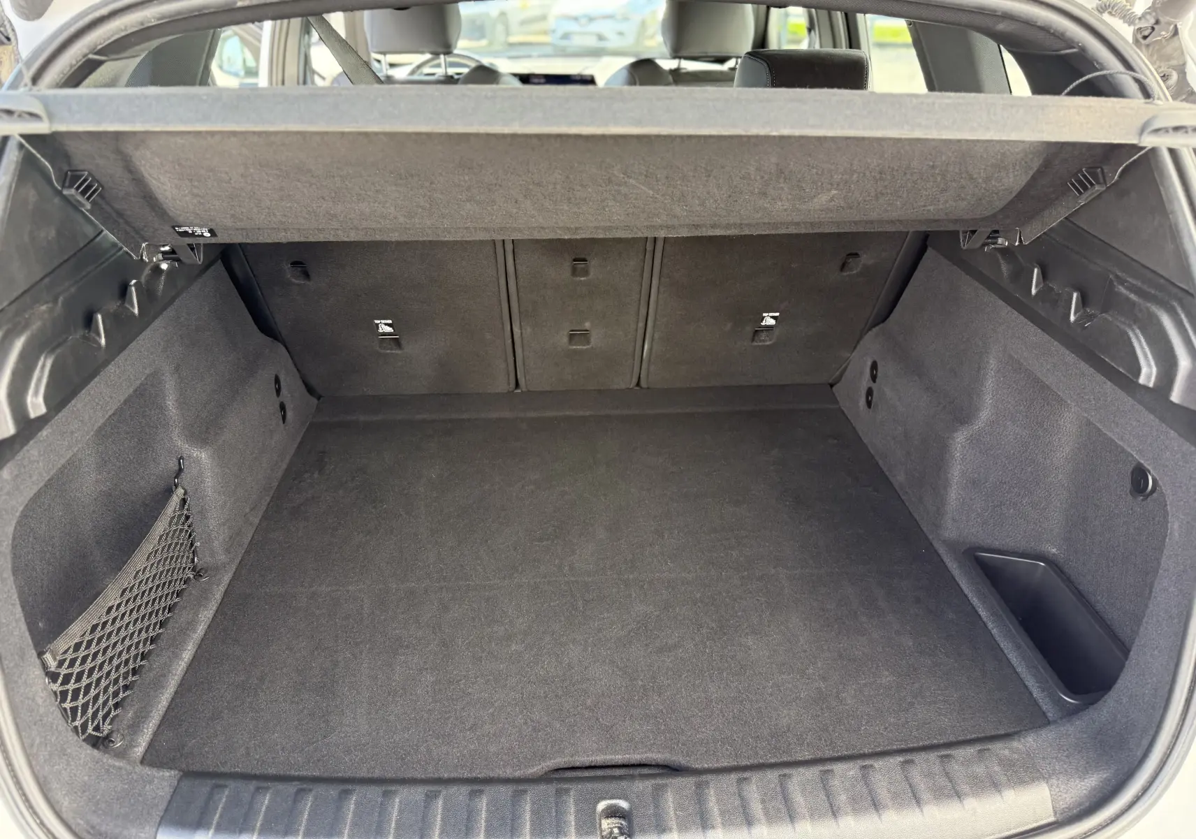 Vue intérieure du coffre spacieux et tapissé de noir du BMW X1 20D 163CH M SPORT blanc minéral, avec filet de rangement latéral.