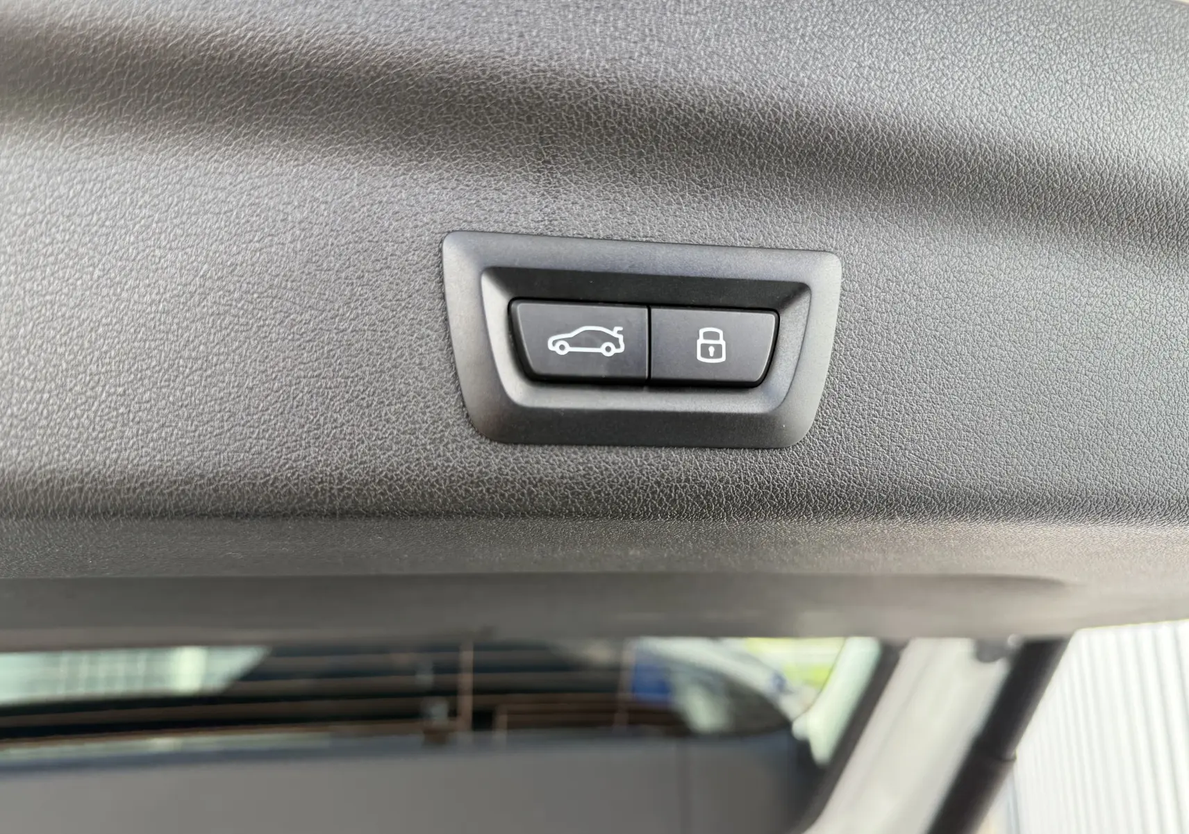 Gros plan sur les boutons d'ouverture et de verrouillage du hayon du BMW X1 blanc mineral, vue intérieure arrière.